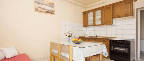 A compact kitchen with wooden cabinets, a dining table with chairs, a small oven, and a painting on the wall.