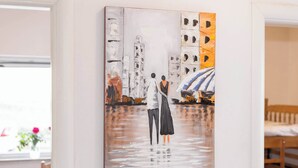 Een schilderij van twee figuren op een brug, met gebouwen en een boot op de achtergrond.