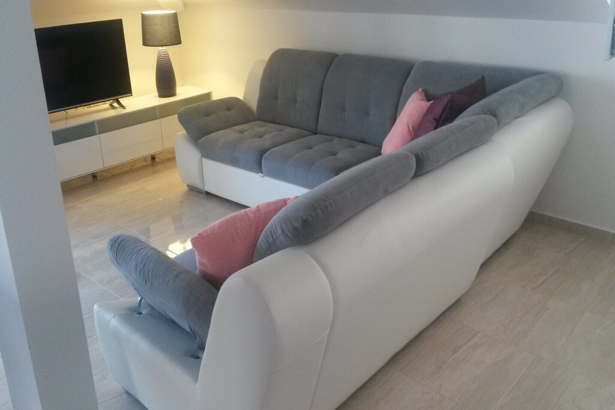 Un soggiorno moderno con un divano grigio, una TV a schermo piatto e una lampada su un tavolo consolle bianco.