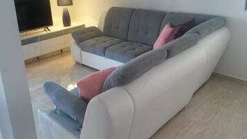 Un soggiorno moderno con un divano grigio, una TV a schermo piatto e una lampada su un tavolo consolle bianco.