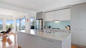 Une cuisine moderne dotée d’un grand îlot central, d’appareils électroménagers en acier inoxydable et offrant une vue sur l’extérieur.