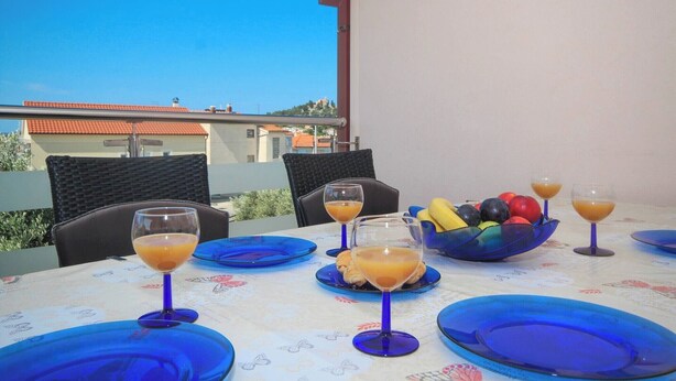 A table set with blue plates, glasses of orange juice, and a bowl of fruit. - Apartment in Tribunj near Tribunj Beach (Tribunj)