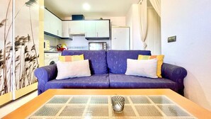 Una sala de estar con un sofá, una mesa de centro y una cocina al fondo.
