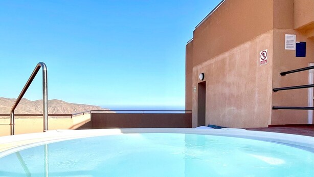 Una piscina con una escalera metálica y vista al mar.