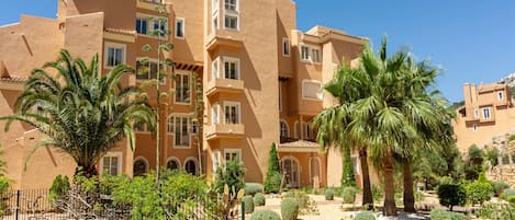 A multi-story building with a courtyard featuring palm trees and a stone pathway.