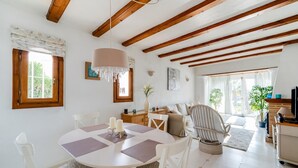 A spacious living area with a dining table, white chairs, a sofa, and a TV stand.
