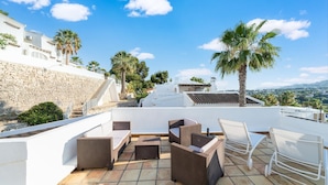 A rooftop terrace with wicker furniture, stone walls, and palm trees.