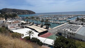 A marina with boats docked, a hill in the background, and a building with a solar panel roof.