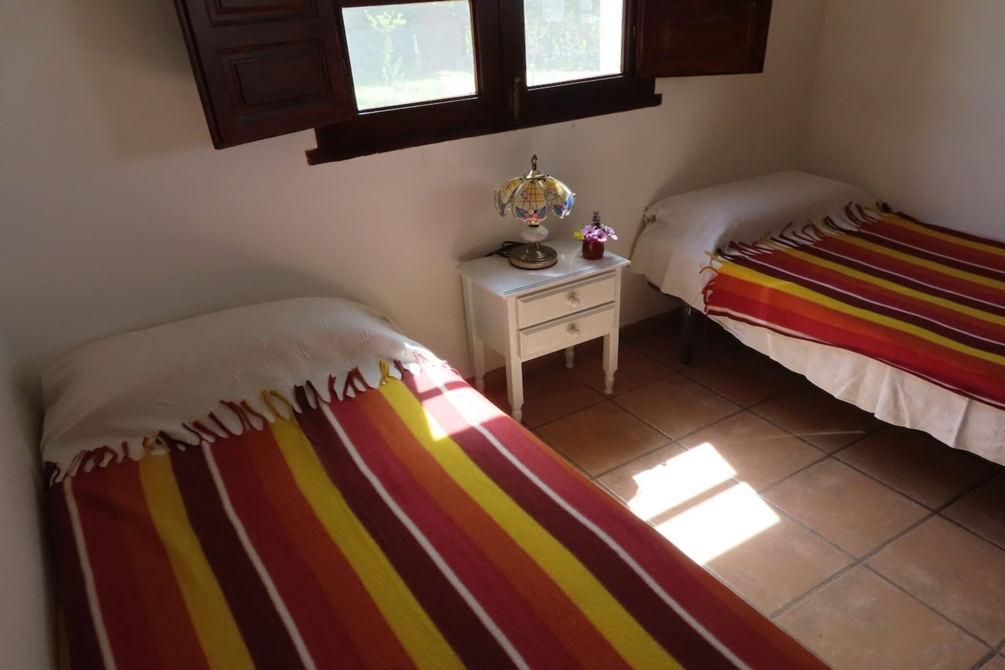 A bedroom with two beds, a nightstand, a globe, and a small vase.