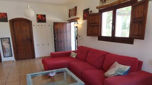 A red sofa with floral cushions, a glass coffee table, and wooden cabinets. - Holiday Home in Orgiva with Mountain Views (Orgiva)