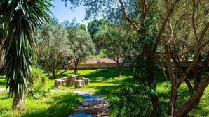 A pathway through a lush garden with trees and a stone structure in the background. - Holiday Home in Orgiva with Mountain Views (Orgiva)