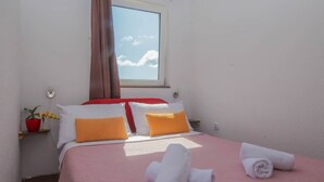 Quarto de hotel com cama, almofadas, janela, planta e toalhas.
