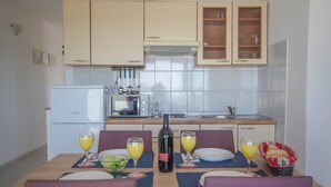 Uma cozinha compacta com geladeira, micro-ondas e pia. Há duas mesas de jantar com cadeiras, cada uma com pratos, copos e uma garrafa de vinho.