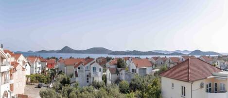 A coastal residential area with houses featuring red-tiled roofs and a view of the sea and distant mountains.