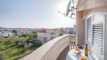 Un balcone con un tavolo apparecchiato per due, affaccia su una zona residenziale con case e vegetazione.