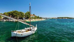A coastal scene with a sailboat docked near a beach, a pier, and buildings in the background. - Apartment in Šibenik near Adriatic Beaches (Šibenik-Brodarica)