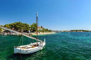 A coastal scene with a sailboat docked near a beach, a pier, and buildings in the background. - Apartment in Šibenik near Adriatic Beaches (Šibenik-Brodarica)