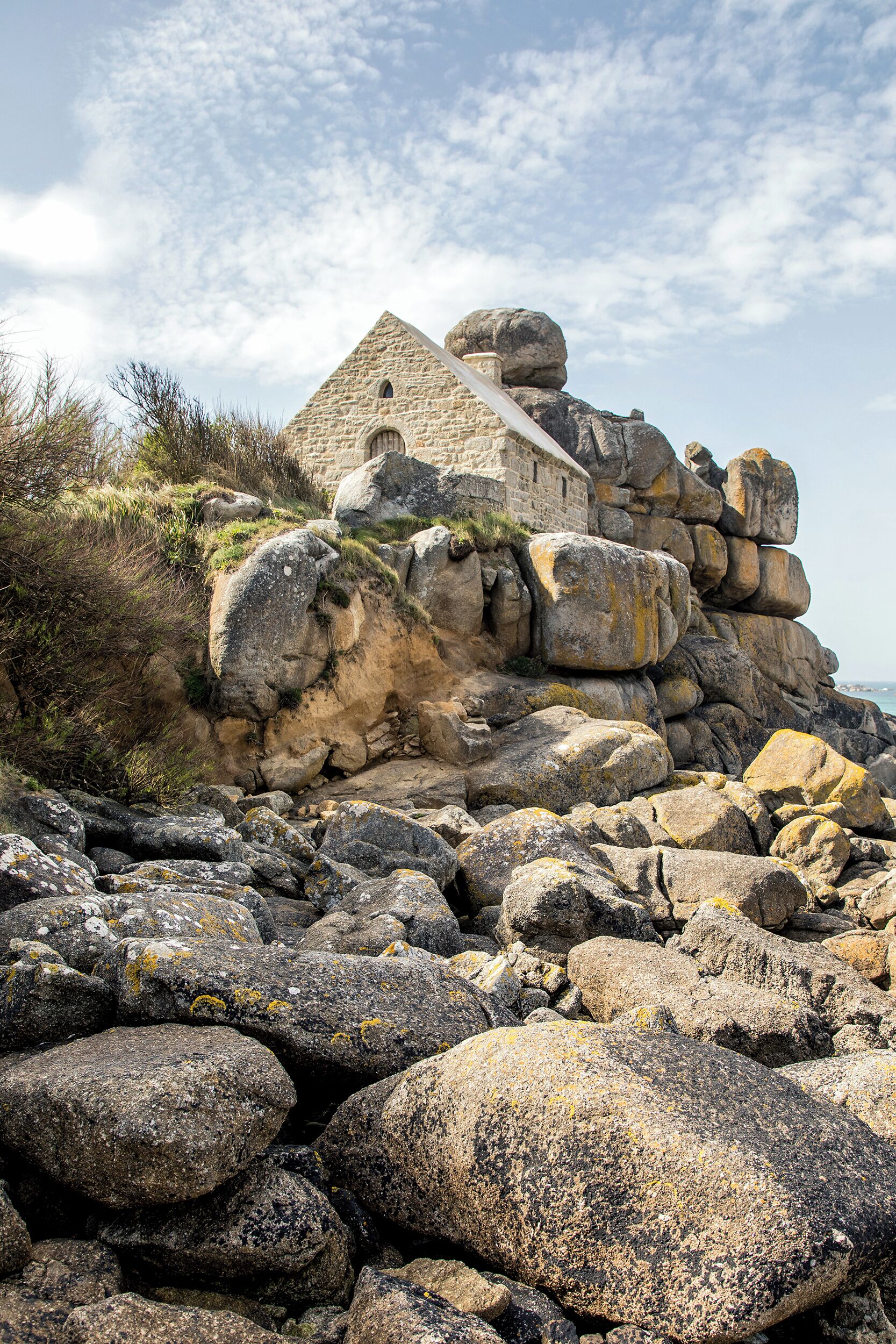 A stone building with a triangular roof, surrounded by large boulders and rocks.