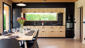 Et moderne køkken med et træspisebord dækket til fire personer, en backsplash i sort marmor og et vindue med udsigt til grøn vegetation.