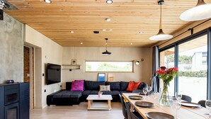 En moderne stue med træloft, en sort sofa, et hvidt sofabord og et spiseområde med et bord dækket til to.