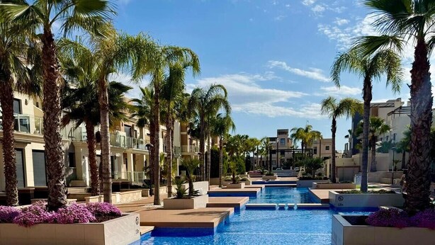 A pool area with multiple swimming pools, palm trees, and a well-maintained lawn. - Ground floor  La Zenia beach, Orihuela Costa (La Zenia)
