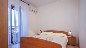 Un dormitorio con una cama de madera, ropa de cama blanca, dos mesitas de noche con lámparas y un equipo de aire acondicionado.