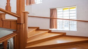 Una escalera de madera con barandilla que conduce a un rellano con ventana y puerta.