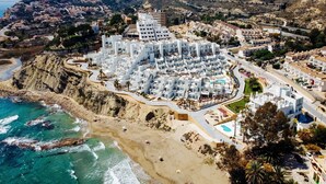 A coastal town with white buildings, a beach, and a mountainous backdrop.