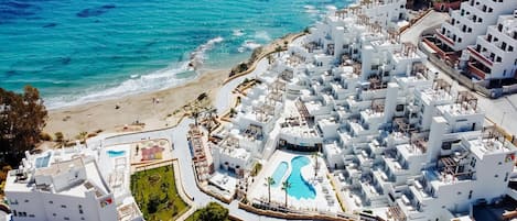 Um resort costeiro com edifícios brancos, uma praia e uma piscina.
