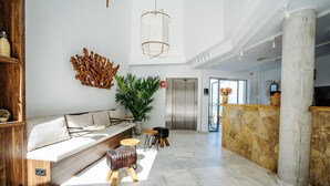 A spacious lobby with a modern sofa, a large potted plant, a wooden bench, and a stone reception desk.