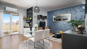 Un salon moderne avec un coin repas, une grande fenêtre avec des rideaux, un téléviseur à écran plat, un panneau indiquant un bar à café et un miroir sur le mur.
