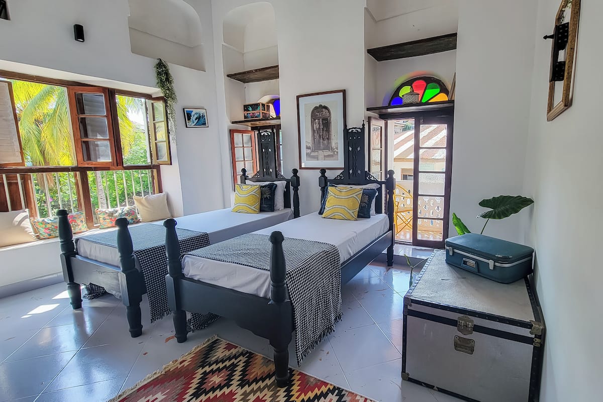 A room with a bed, a small desk, a suitcase, and a window with a view of greenery.