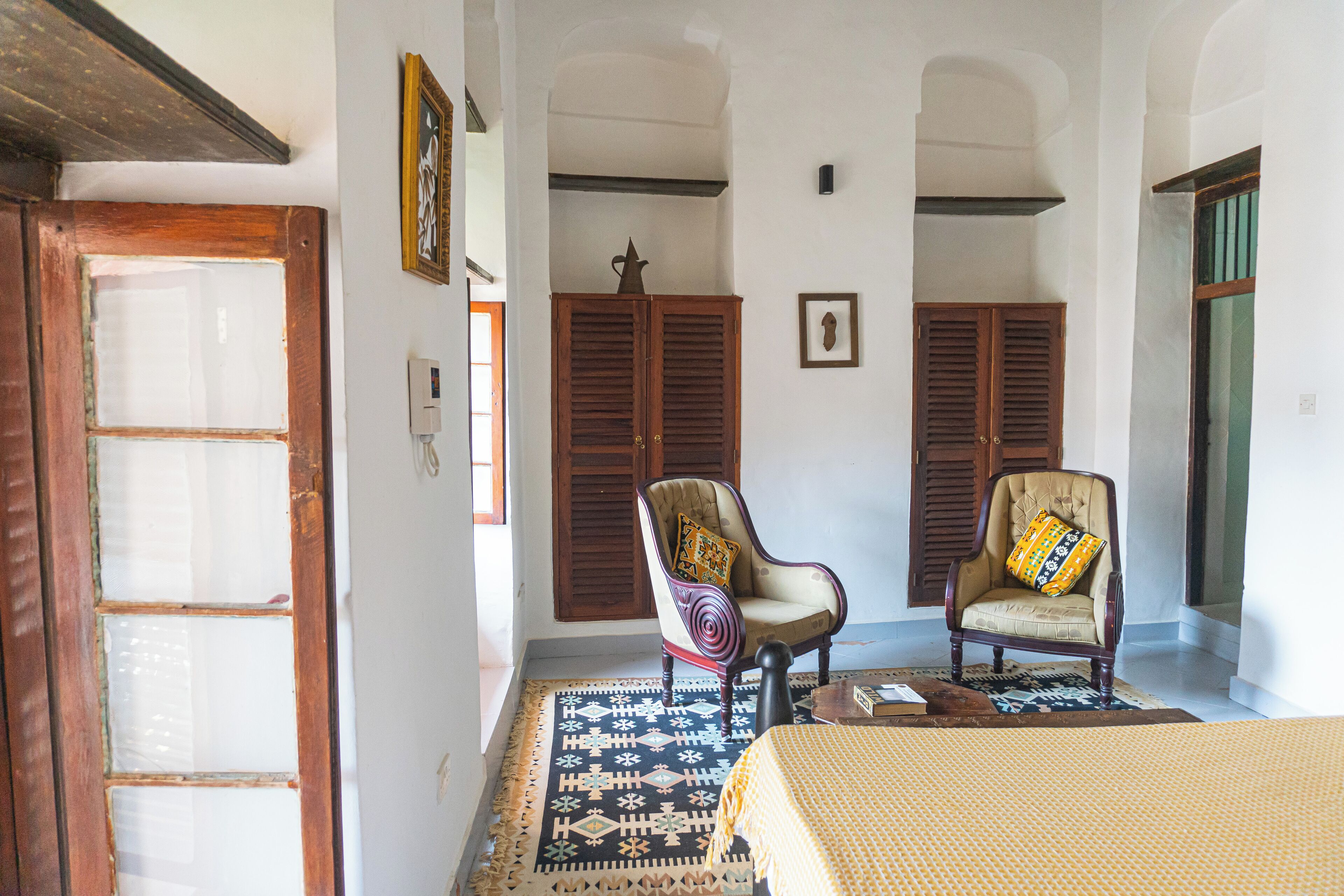 Une pièce comprenant un lit, deux fauteuils, un tapis, des portes en bois et un tableau accroché au mur.