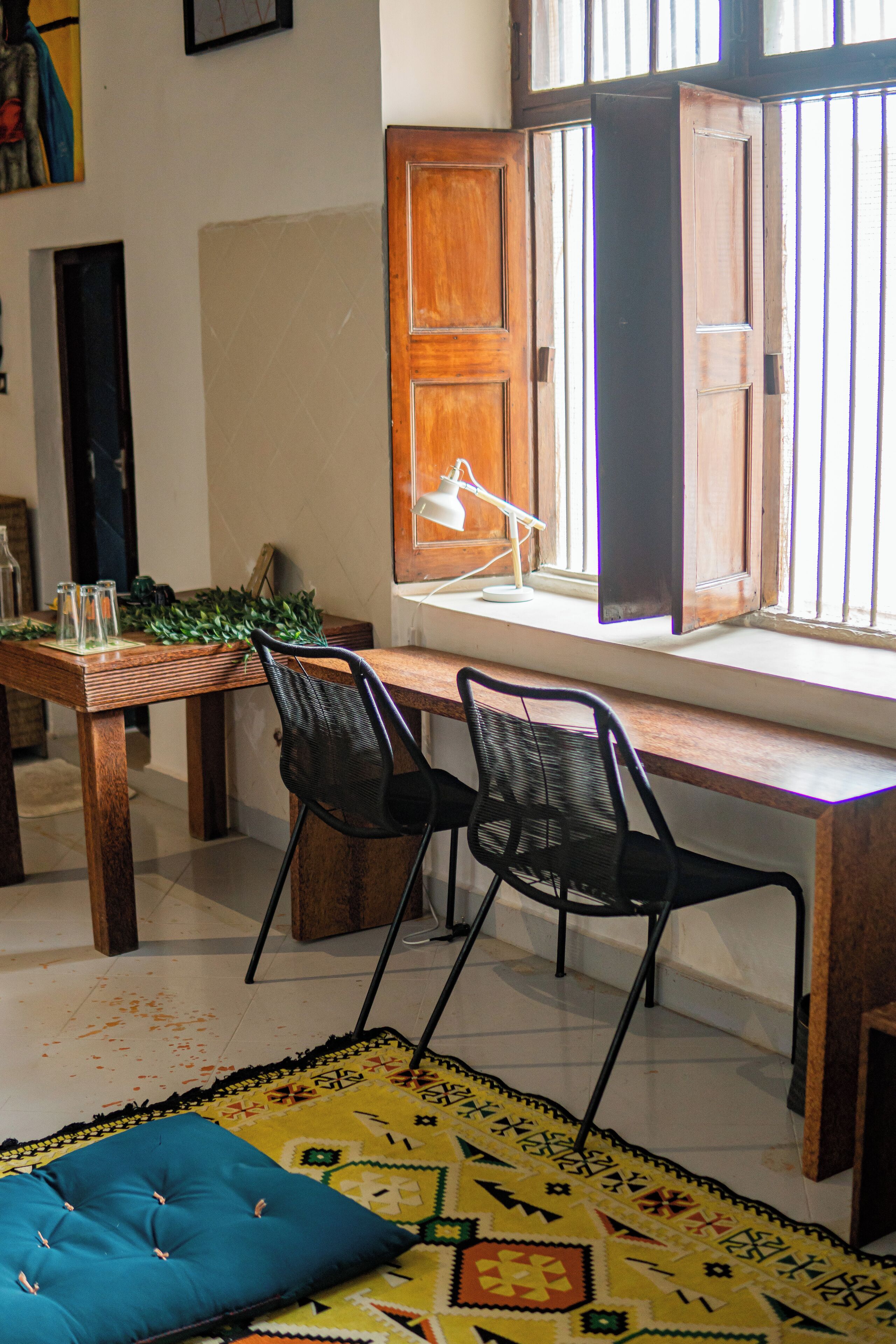 Un comedor con una mesa de madera, dos sillas negras, un banco acolchado azul y un tapiz estampado.