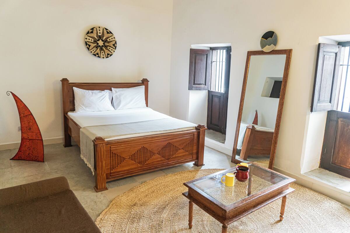 A bedroom with a wooden bed, a glass coffee table, a woven rug, and a wall clock.