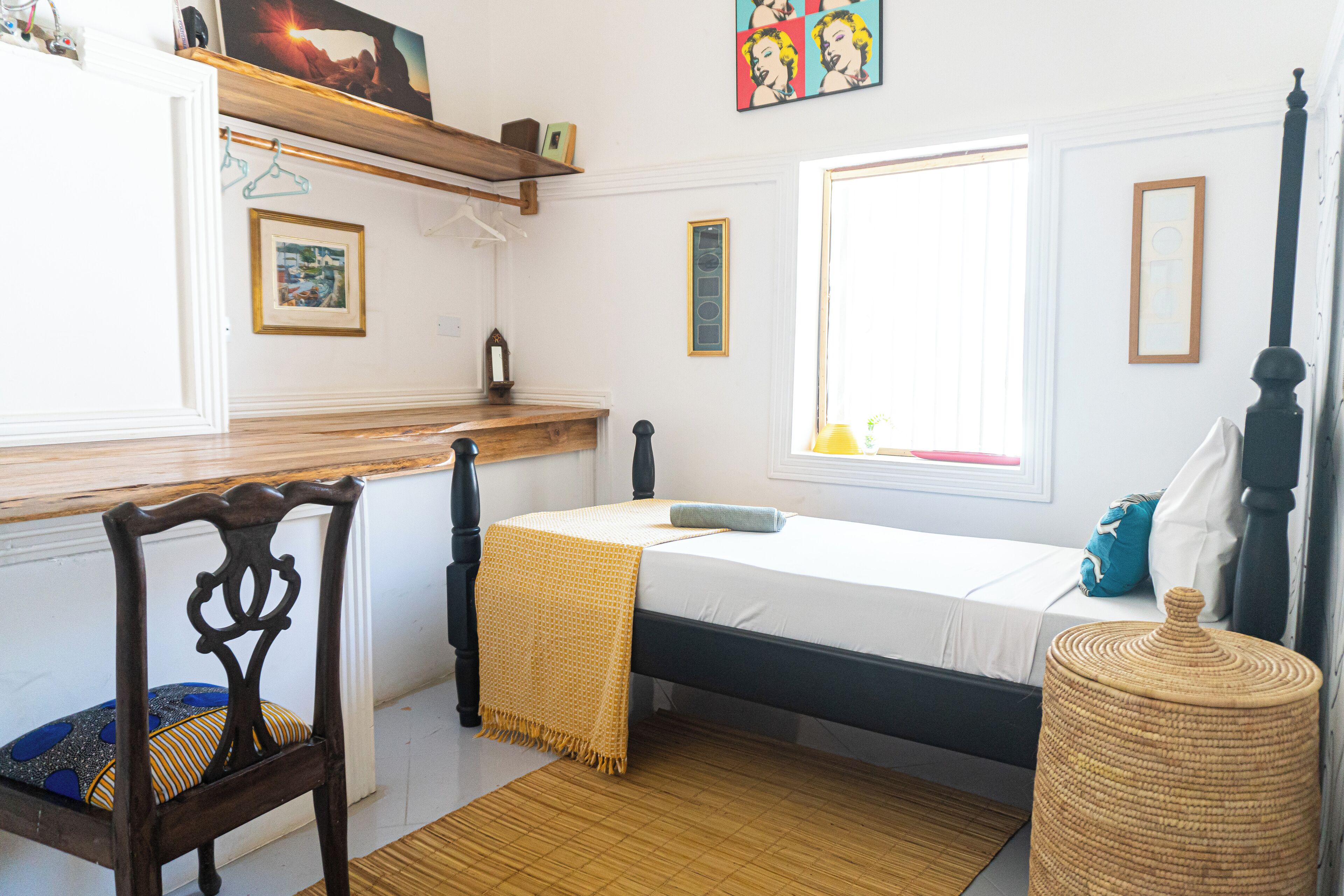 A bedroom with a bed, a chair, a window, and a shelf with items.