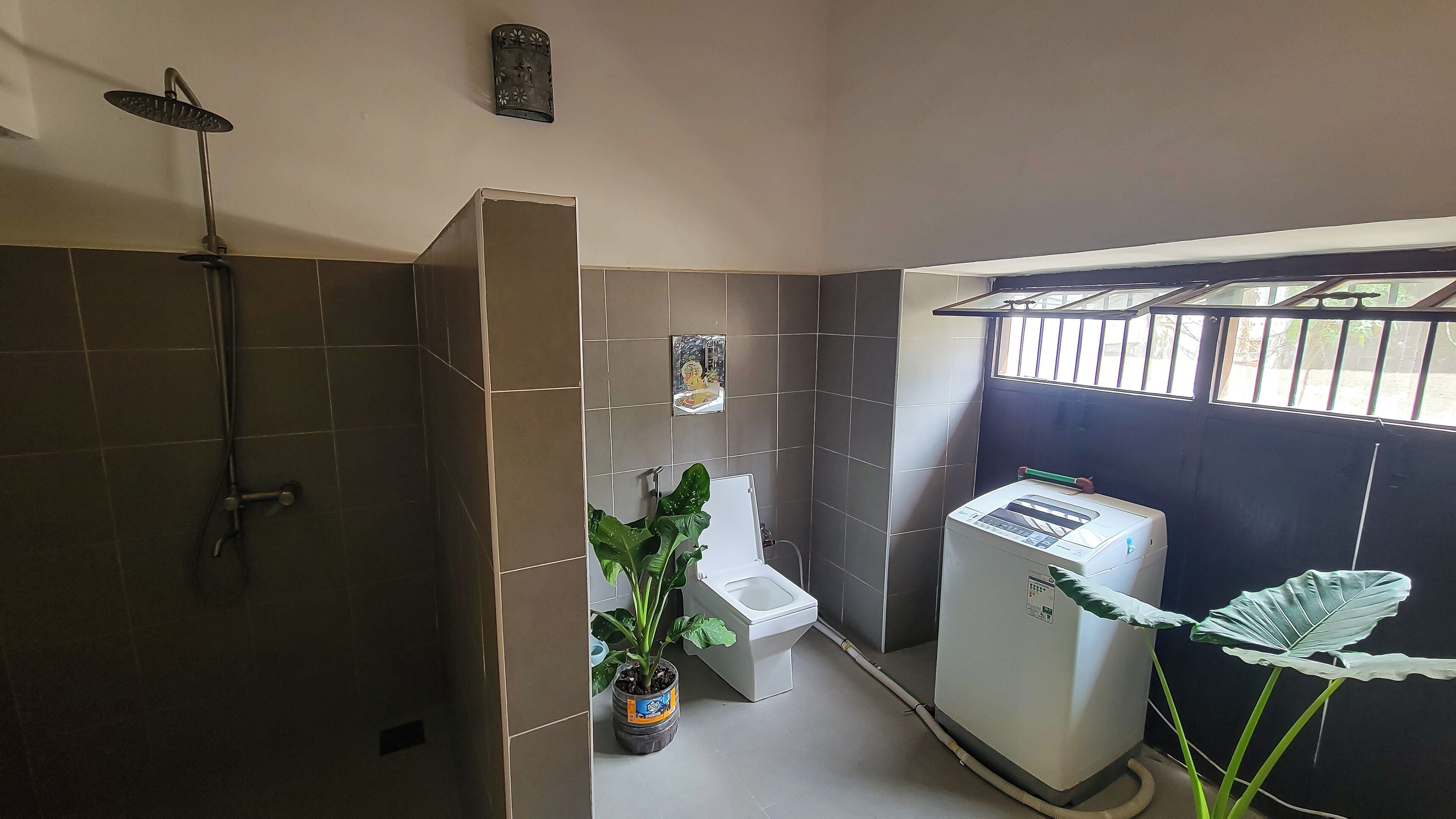 Un baño pequeño con ducha, inodoro y lavadora compacta.
