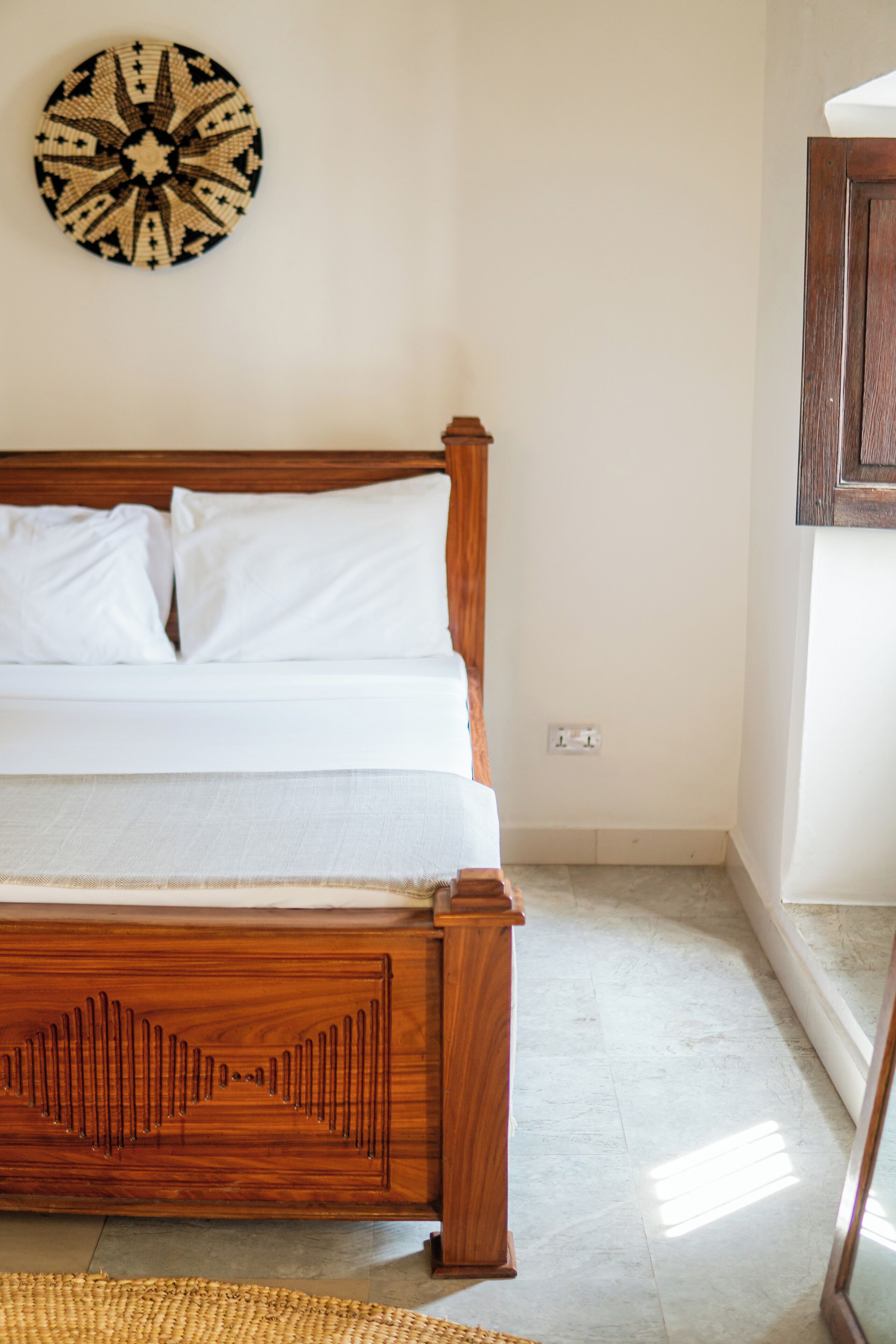 A bed with a wooden frame, white bedding, and a woven rug.