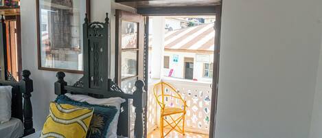 A bedroom with a bed, a nightstand, a mirror, and a window with a view of the outside.