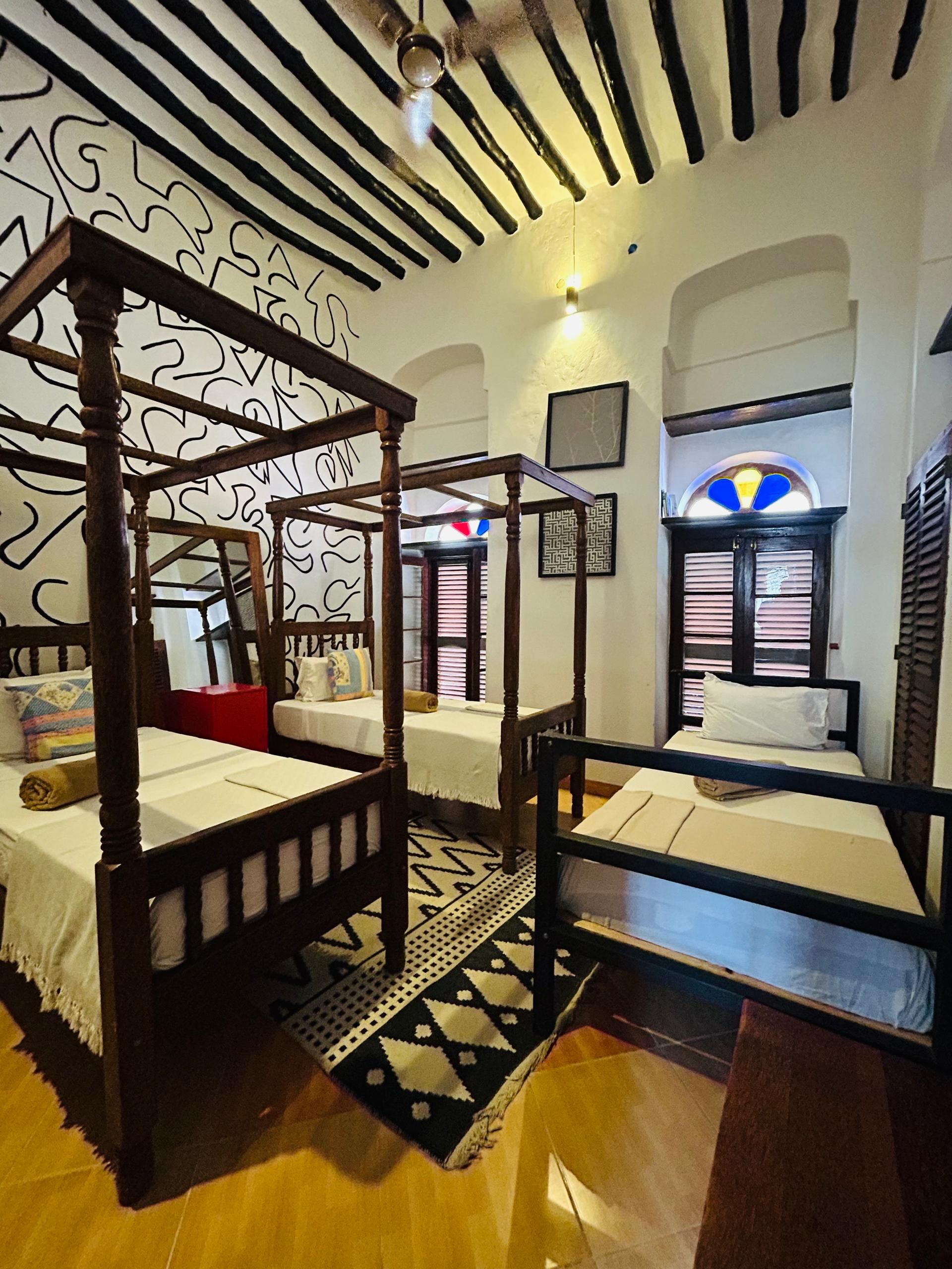 Una habitación con una cama con dosel, una cama individual y una cama chaise longue. Hay una alfombra estampada en el suelo.