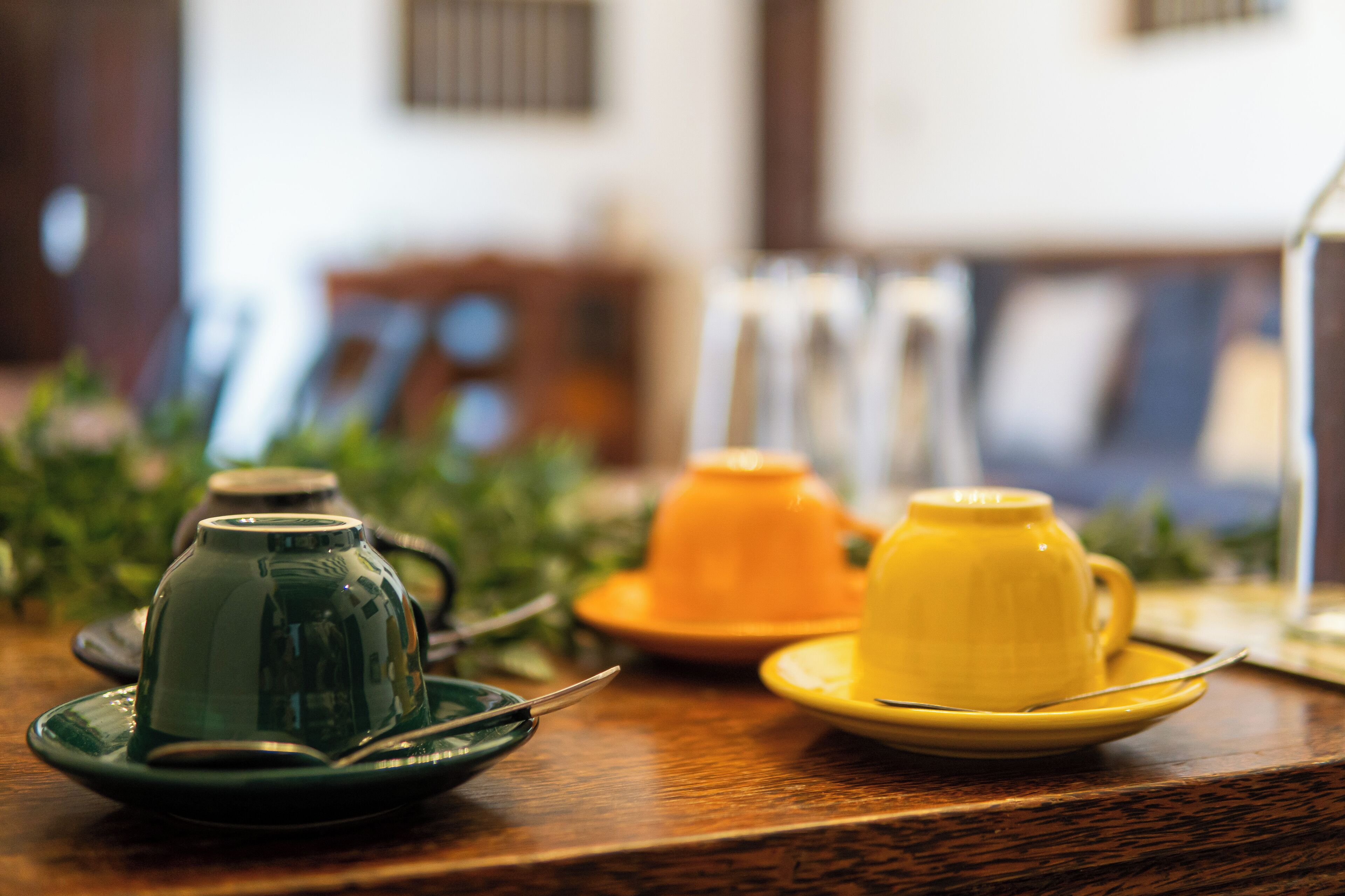 A table with a green teapot and a yellow cup on saucers, with a spoon on each.