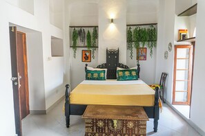 A bedroom with a bed, a bench, a door, and hanging plants. - Tarawanda House By Stawi (Zanzibar Town)