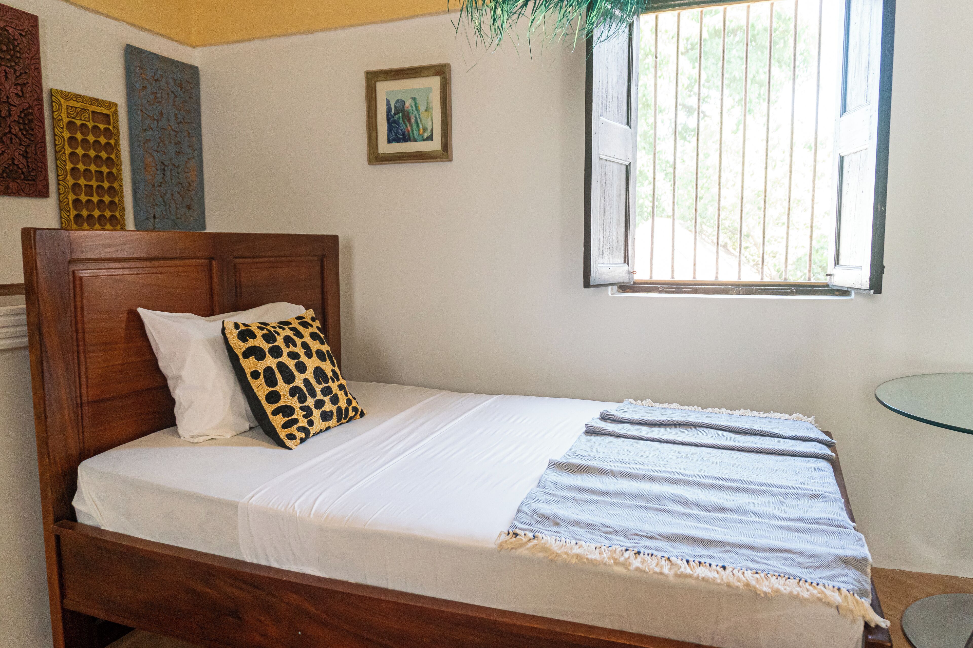 Una cama bien tendida con cabecera de madera, colchón blanco y almohada estampada.