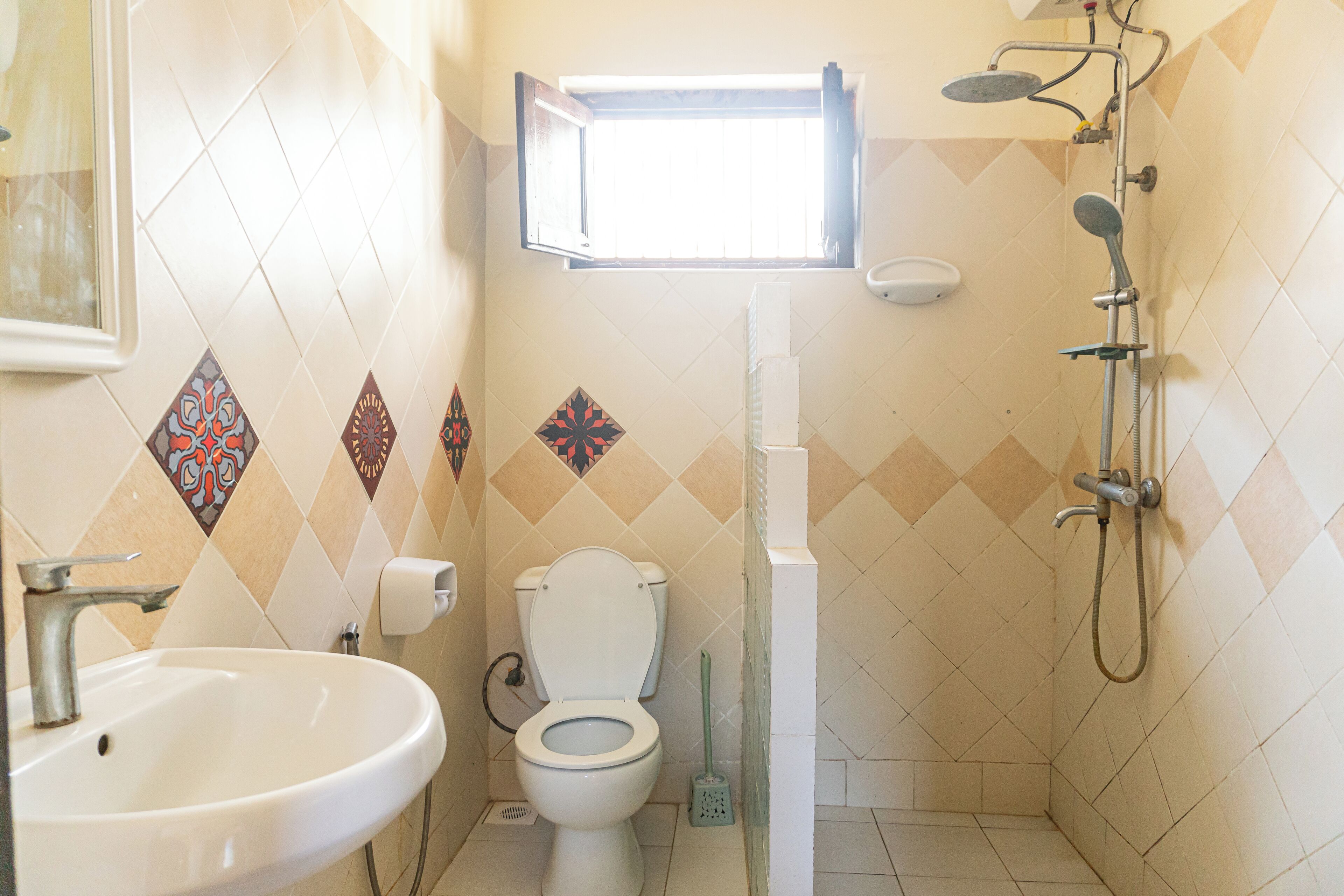 A bathroom with a toilet, sink, shower, and a window above the toilet.