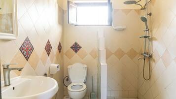 Un baño con inodoro, lavamanos, ducha y una ventana sobre el inodoro.