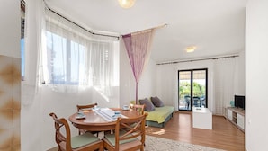 A cozy living room with a wooden dining table, a sofa, and a TV. - 2 persons apartment with garden (Šibenik-Brodarica)