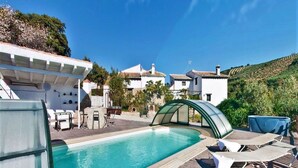 A swimming pool with lounge chairs and a covered area, surrounded by buildings and greenery. - Country House in Andalusia with Pool (Andalucía)