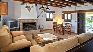 A cozy living room with a fireplace, a sofa, a coffee table, and a dining area with chairs and a table. - Country House in Andalusia with Pool (Andalucía)