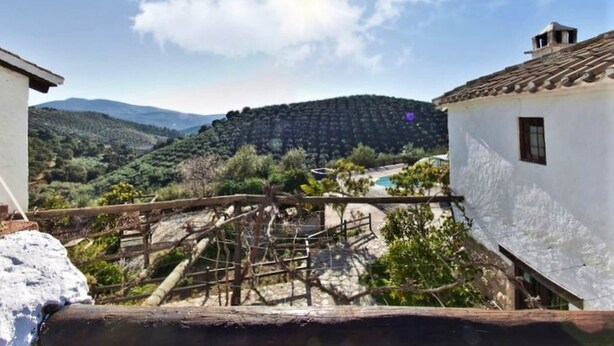 A rustic building with a white exterior, a wooden staircase, and a view of a hilly landscape with a clear sky. - Country House in Andalusia with Pool (Andalucía)