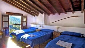 A room with two beds, wooden beams on the ceiling, a window with a view of a mountain, and a small table with a lamp. - Country House in Andalusia with Pool (Andalucía)